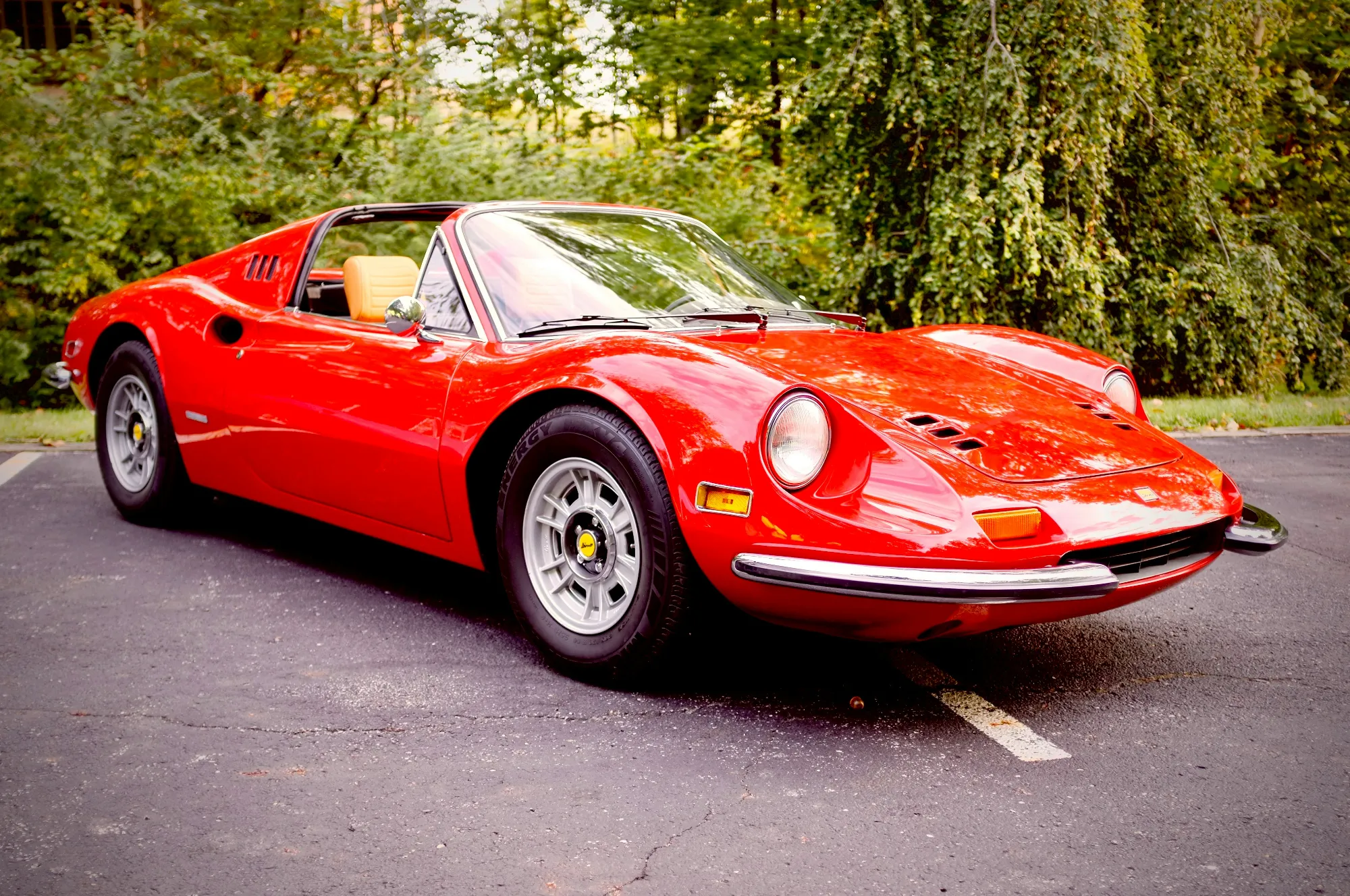 A red classic Ferrari Dino parked by the trees